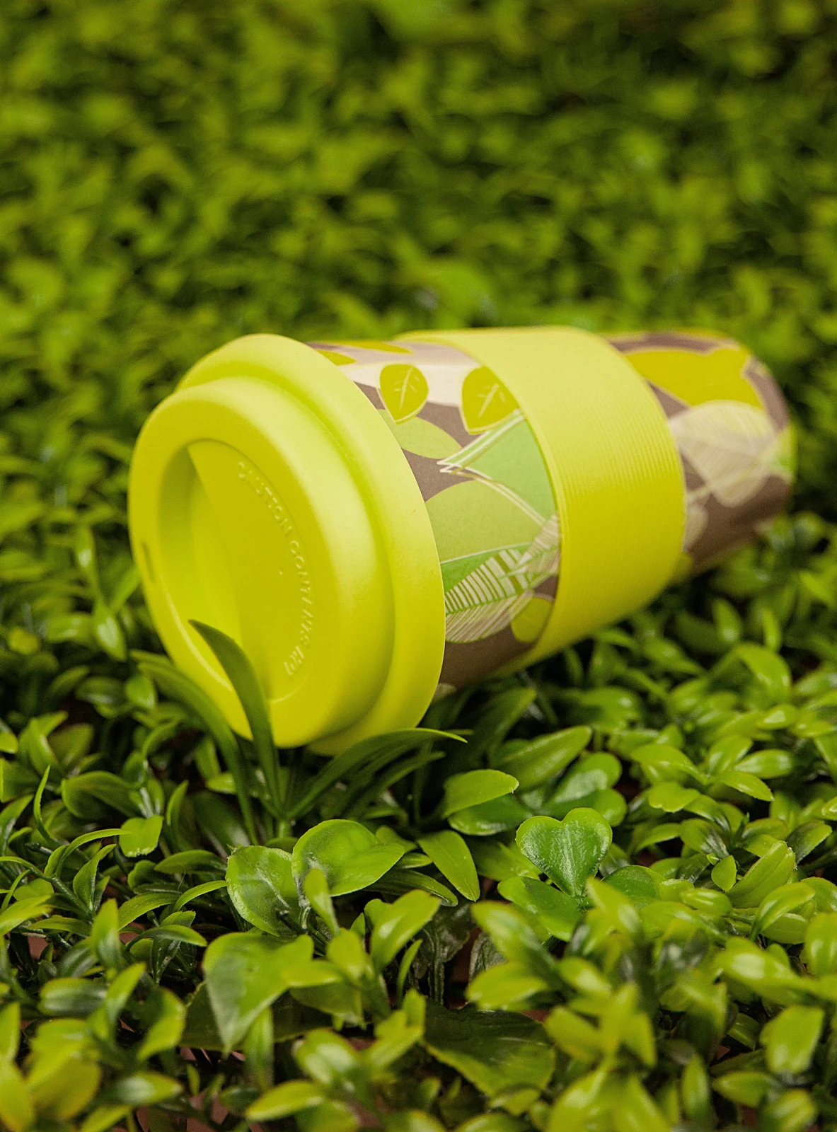 Een herbruikbare beker met groen deksel tussen groene bladeren